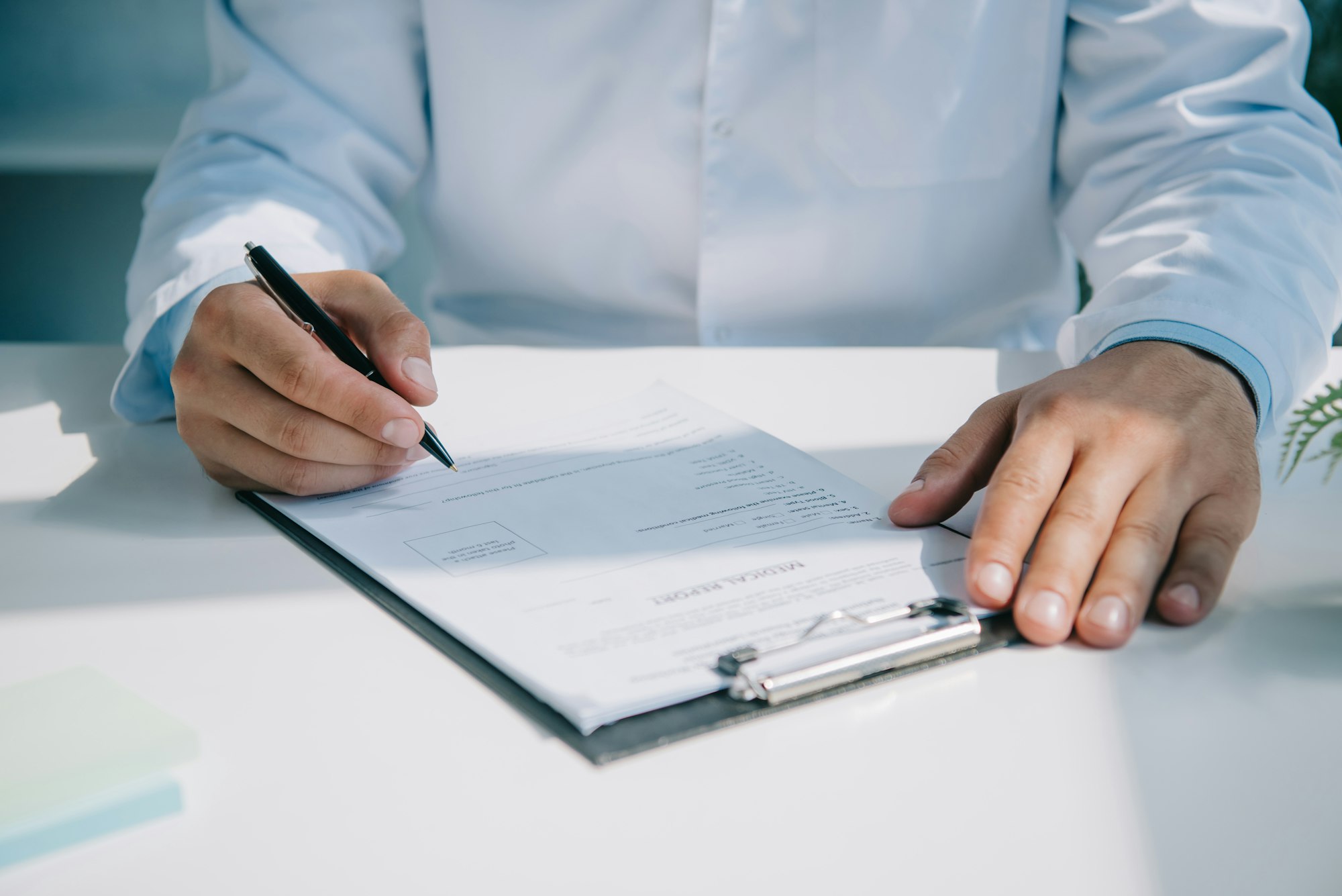 partial view of doctor writing diagnosis in medical report on clipboard
